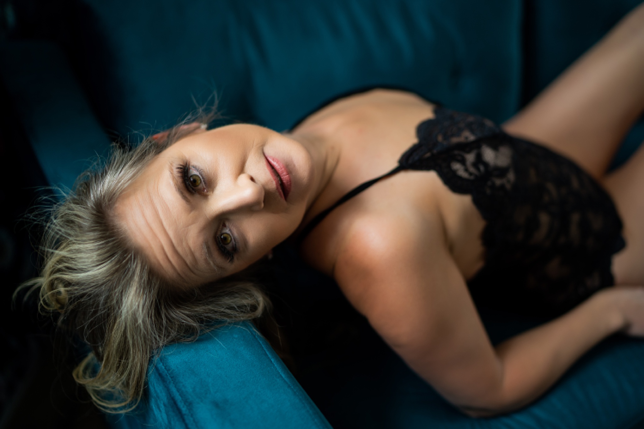 Woman in black lingerie laying on blue couch Sereni Salon